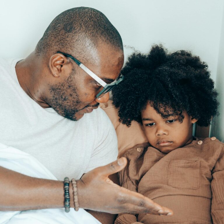 Father and child in bed, discussing and playing with a gamepad, fostering connection at home.