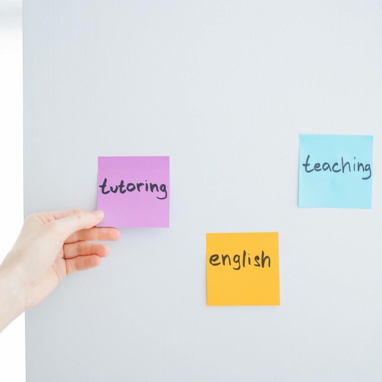 Hand placing sticky notes with words tutoring, teaching, and English on a wall, ideal for educational content.