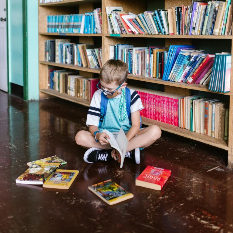 A child enjoys reading books inside a library, surrounded by shelves.