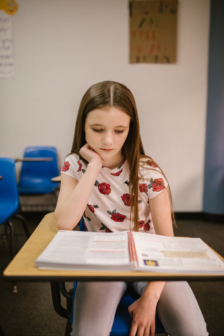 Young girl in a classroom reading a textbook. Focused and contemplative.