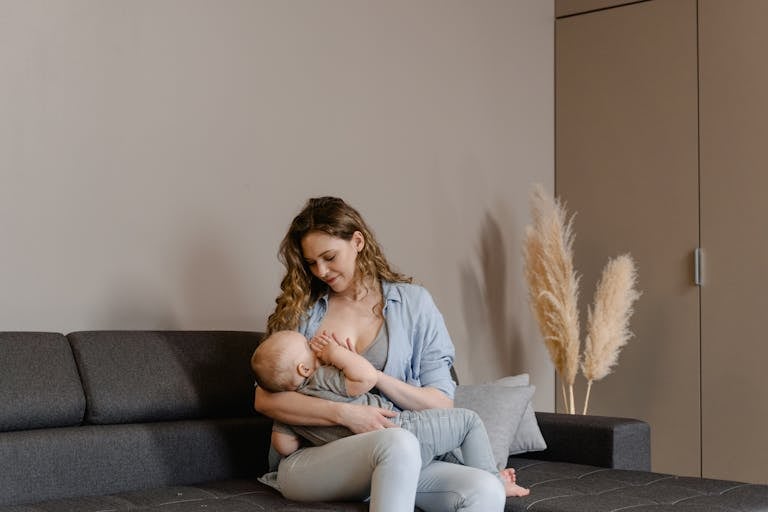A tender moment of motherhood as a mother breastfeeds her baby on a sofa, indoors.