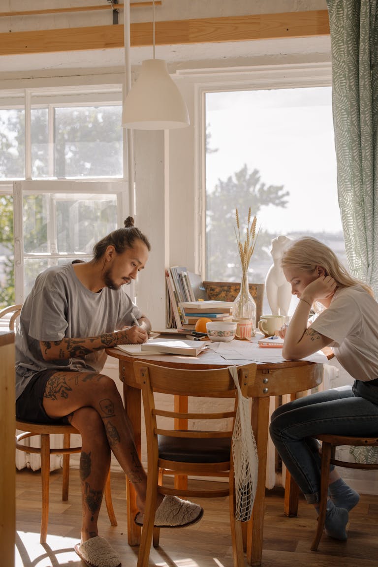 Two young adults engage in study at a sunlit table, creating a serene learning environment.