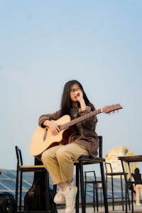 A woman sitting on a chair playing guitar at sunset in an outdoor setting.