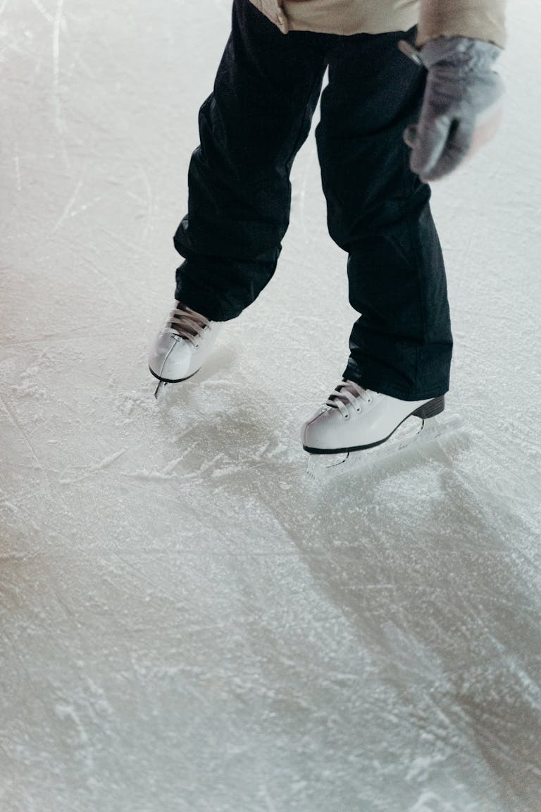 Close-up of legs in black pants and ice skates on a rink.