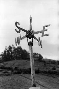 A classic weather vane in a rural field with blurred landscape background.