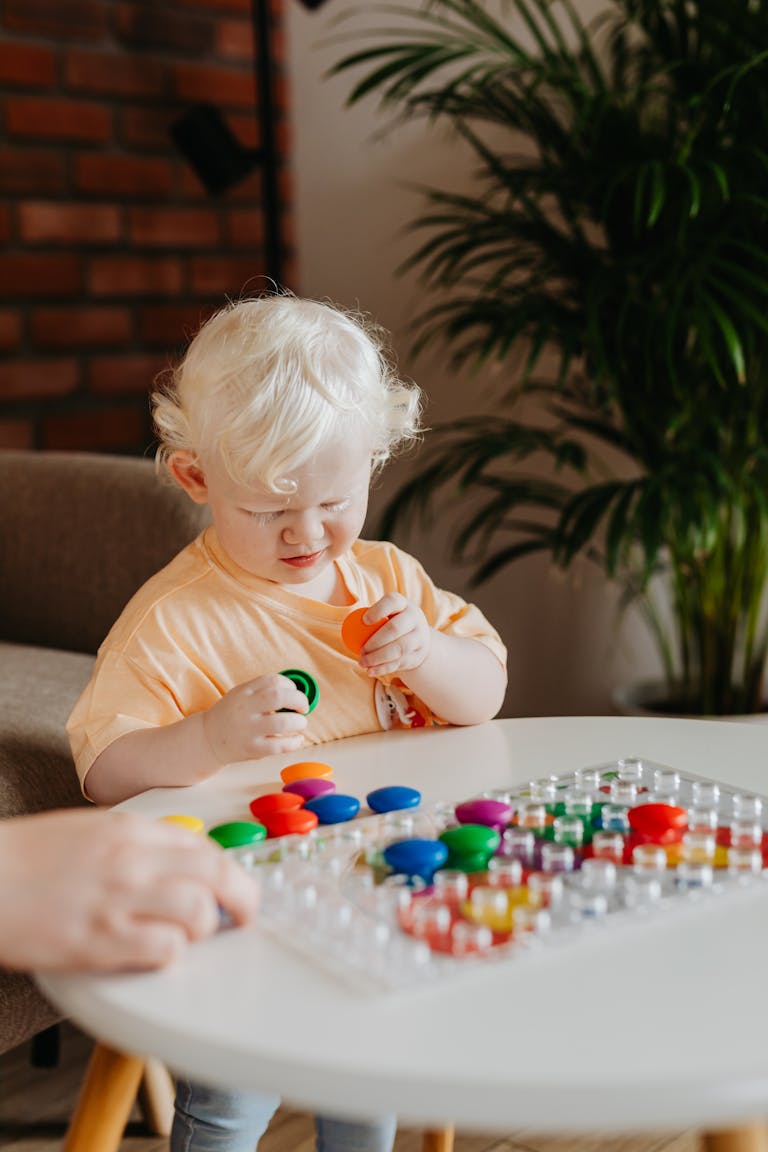 A toddler playing with colorful toys at a table indoors, capturing a moment of childhood discovery.
