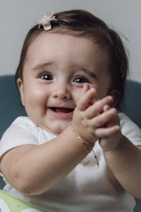 Charming baby girl clapping hands joyfully in an indoor setting, with a cute smile. Perfect for lifestyle and family themes.