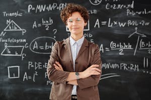 Confident female teacher standing with arms crossed in front of a detailed mathematical blackboard.