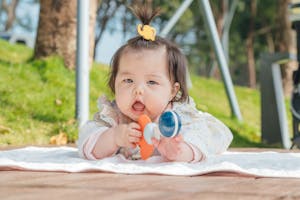 Cute Asian baby enjoying playtime on a blanket outdoors with a toy.