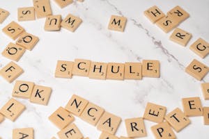Scrabble letter tiles spelling 'Schule' on a marble surface, ideal for language learning concepts.