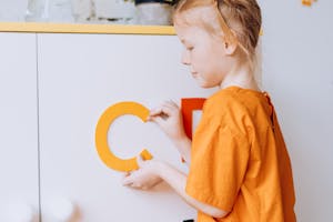 A girl in an orange shirt arranging colorful letters, promoting creativity and education.