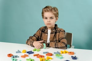 A young boy in a plaid shirt sits at a table with colorful alphabet letters on a blue background.