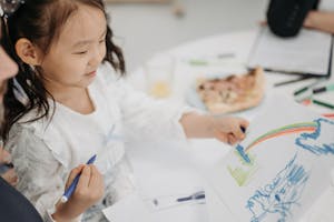 A young girl happily draws a colorful rainbow using pencils, showcasing creativity and imagination.
