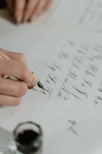 Close-up of a hand writing calligraphy with a fountain pen, showcasing elegant script.